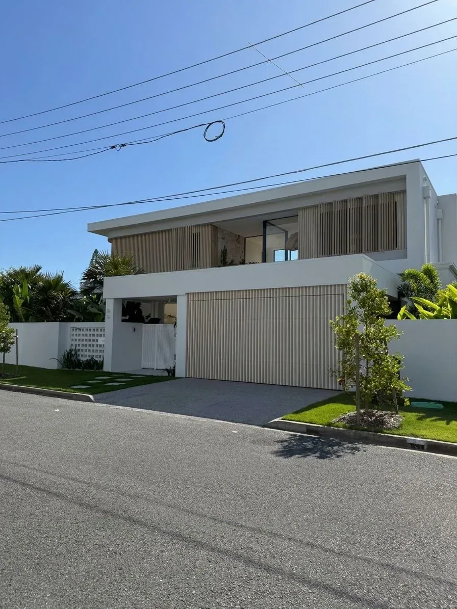 A contemporary two-storey home in Miami, Gold Coast, with white rendered walls, timber-look vertical slats and a slatted garage door