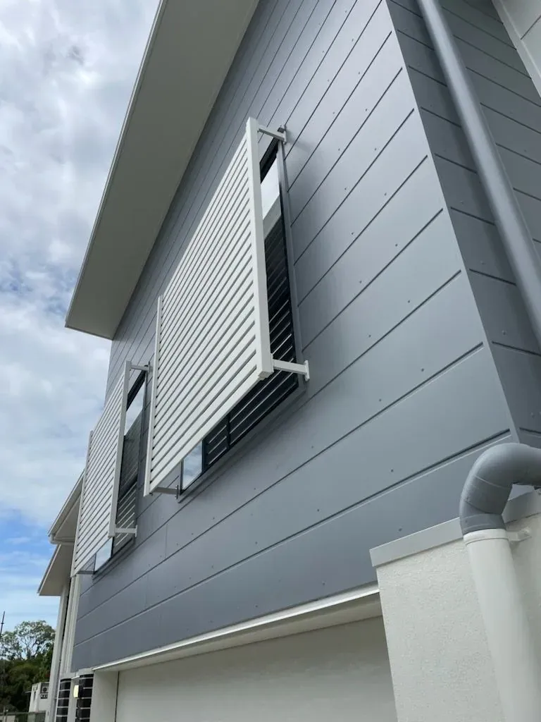Grey painted cladding on a two-storey Brisbane home with white louvre shutters over the windows