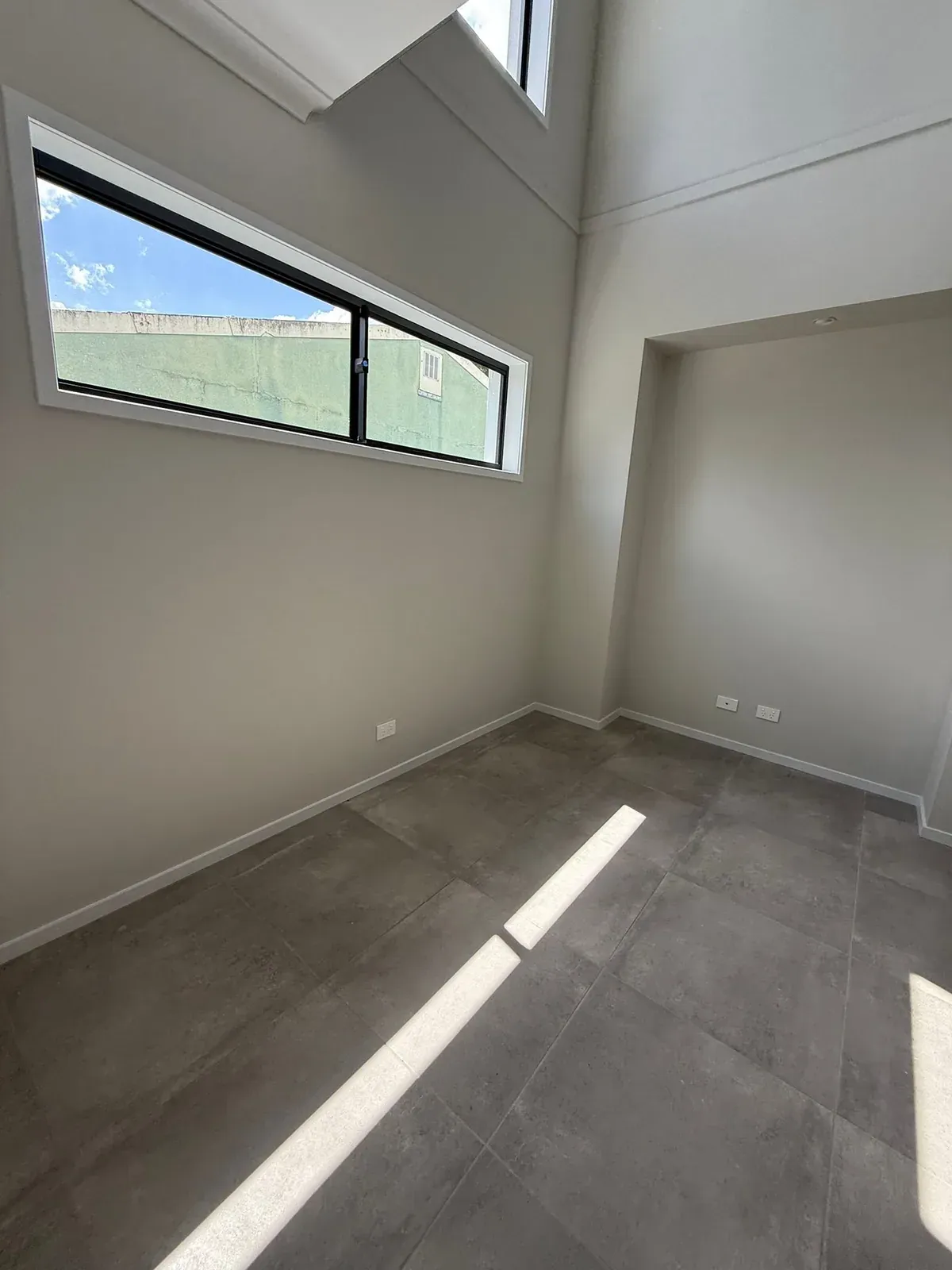 A bright room in Salisbury, Brisbane, with a high ceiling, freshly painted warm grey walls, white trim and a tall window