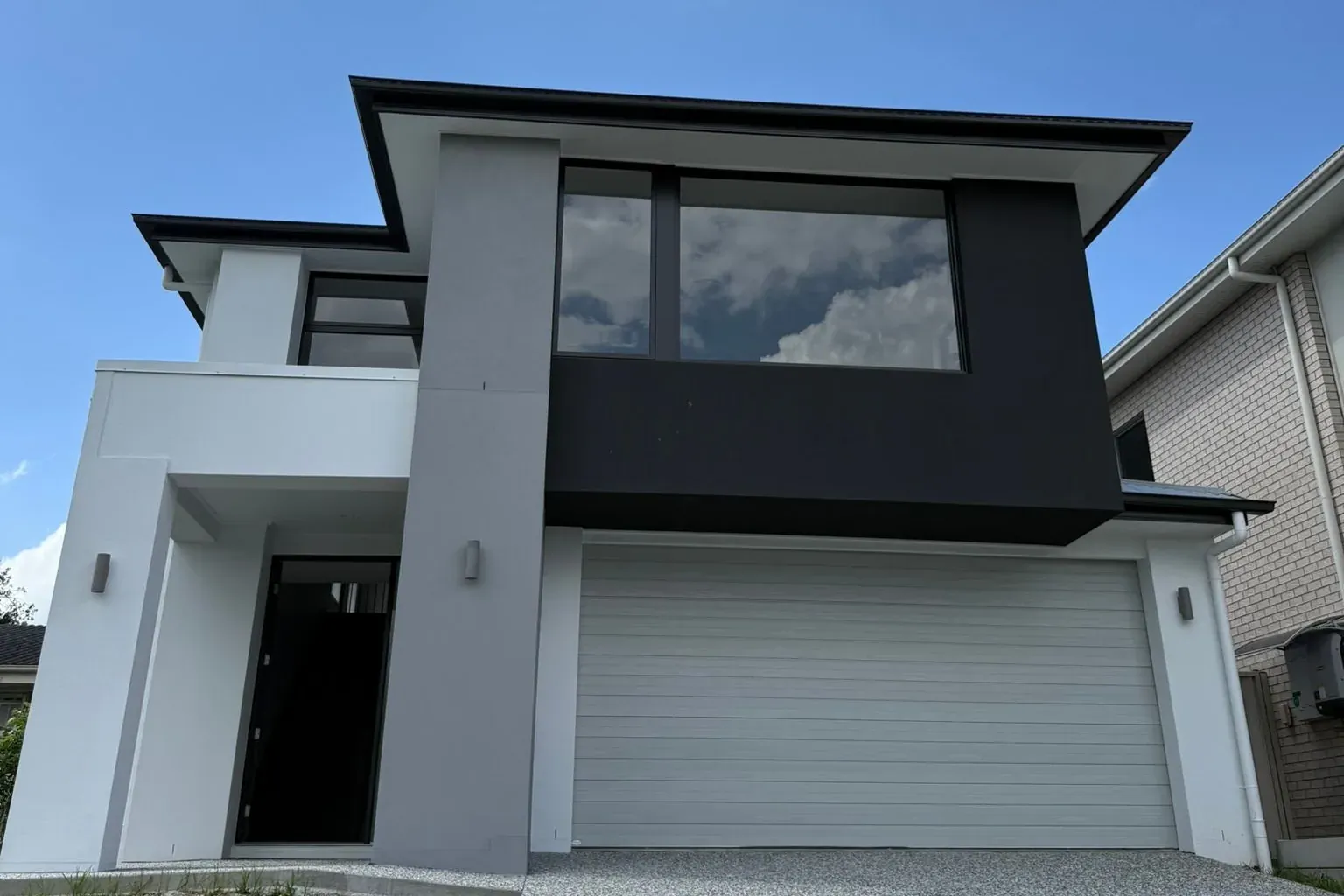 A two-storey home in Salisbury, Brisbane, with grey and white rendered walls, a black feature box around the upstairs window and a white garage door, freshly painted by AnB