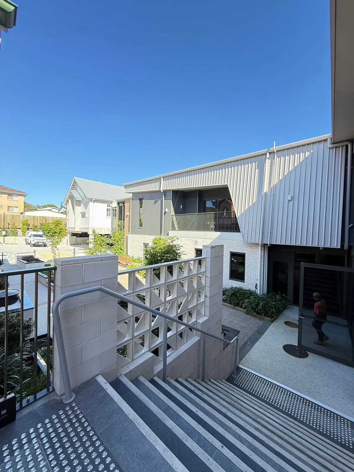 The courtyard of a modern multi-residential building in Annerley, Brisbane, with painted white brick, grey cladding and a breeze block wall beside the steps