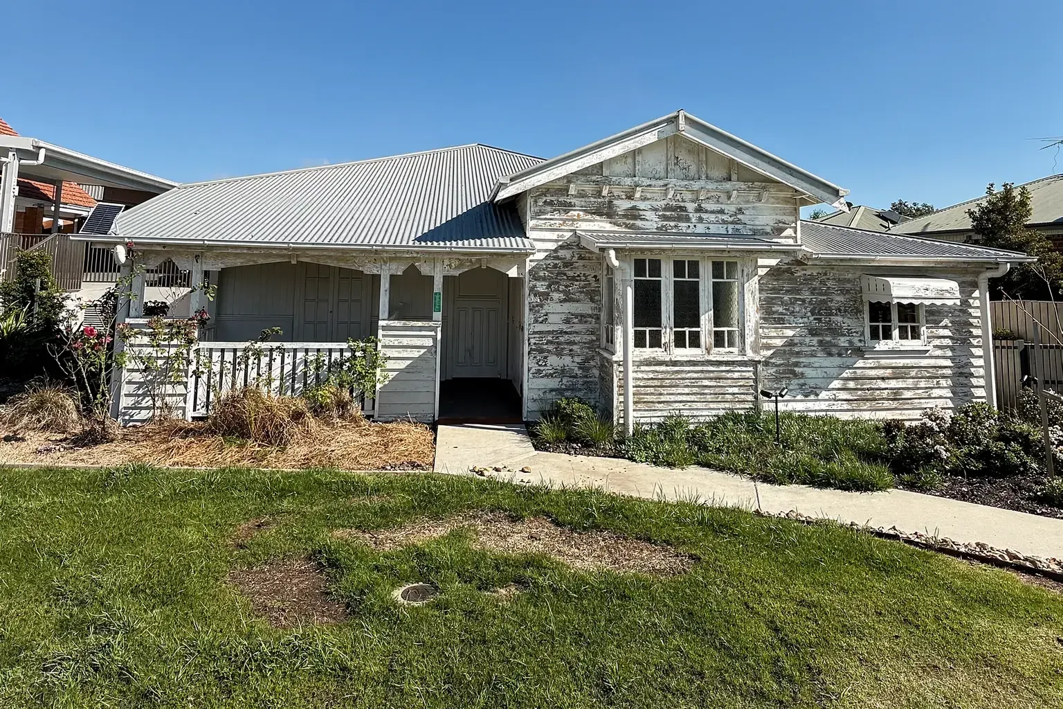 A Queenslander home with faded, flaking paint, dirty trims and a long lawn before repainting